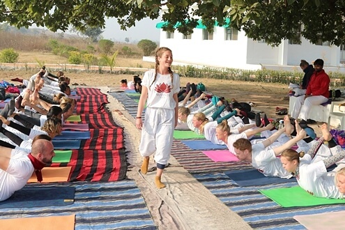 Students are performing Bow pose, an outdoor asana during YTT Students practicing bow pose in an outdoor setup