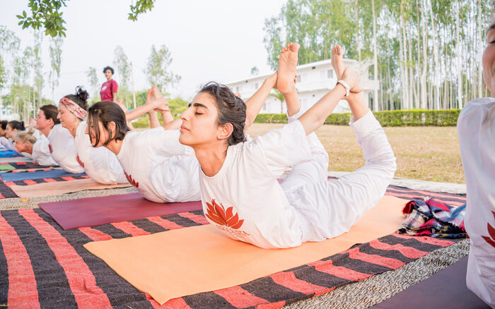Group of Yoga Teacher Trainees holding Bow pose in Ashram Ground in India YTT students practicing Bow pose together in an outdoor setup