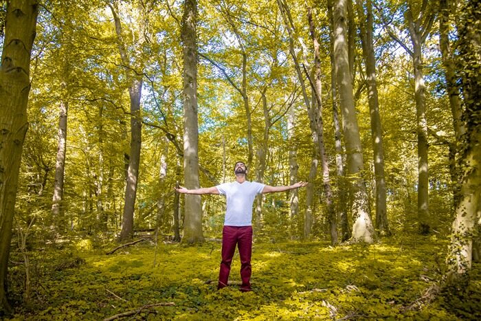 A yoga practitioner stands in nature with his arms held out