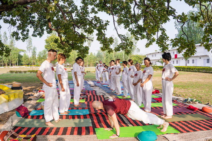 A yoga teacher instructs students in a yoga class outside