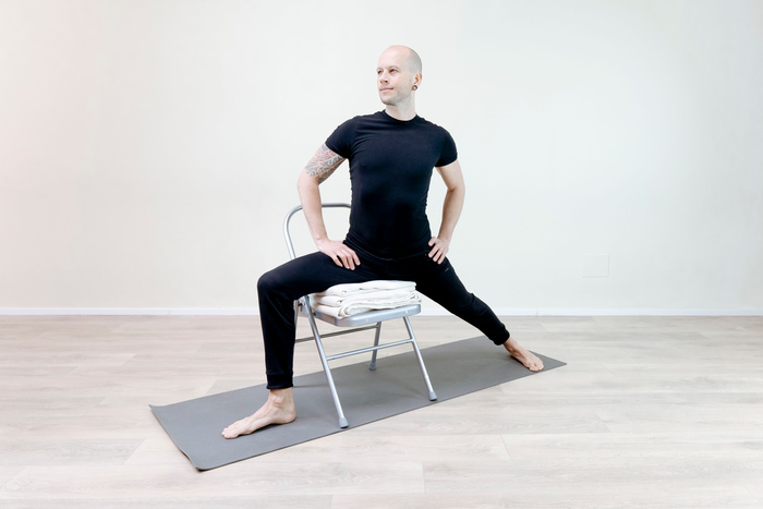 A man practices Warrior Pose with the support of a chair A man practices Warrior Pose with the support of a chair