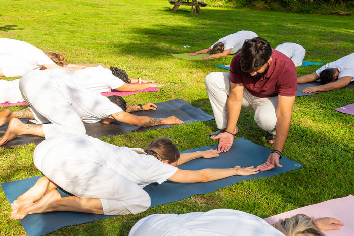 Students practicing a wide-knee Frog Pose hip opener during an outdoor Yin Yoga class under yoga teacher’s guidance