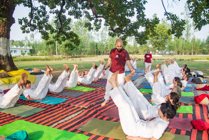 Students practicing yoga outdoors Yoga teacher guiding students through a core strengthening posture during an outdoor session