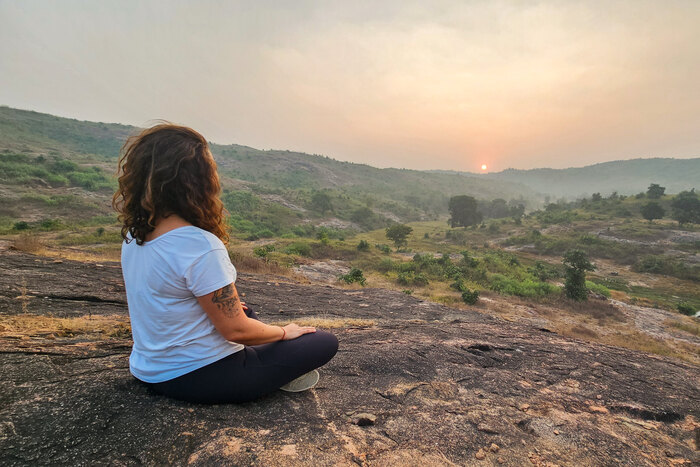 Woman meditating alone in the Sukhasana easy pose on a rocky hilltop Woman meditating alone in the Sukhasana easy pose on a rocky hilltop
