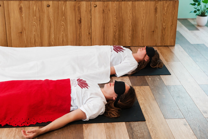 Two women practicing Yoga Nidra with eye masks and blanket Two students lying in Shavasana practicing Yoga Nidra with eye masks